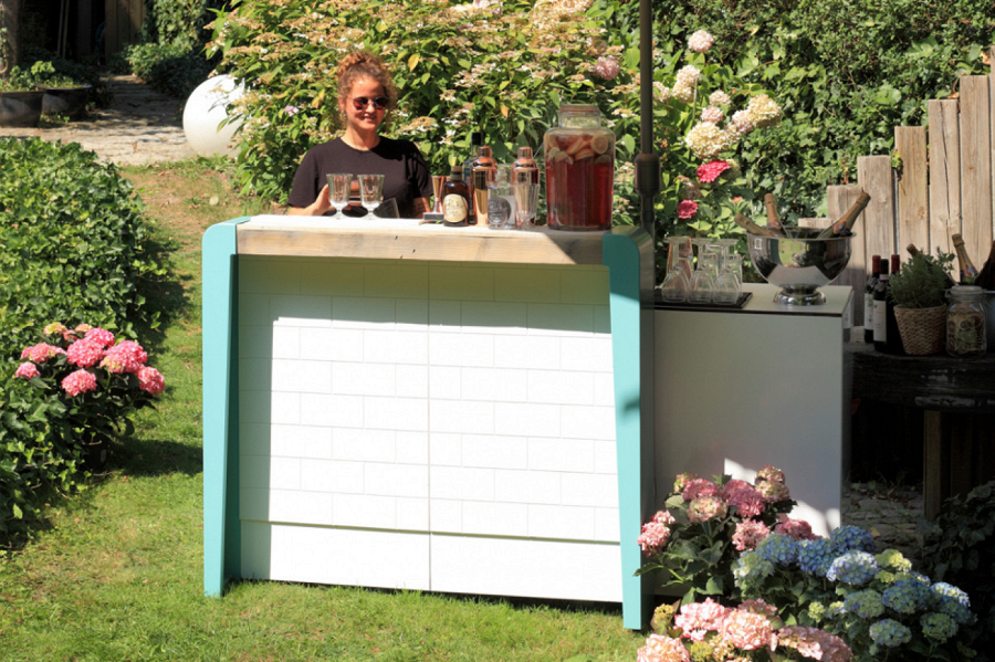 Balcão de cocktail móvel com aspeto de azulejo, madeira e aplicações laterais em azul claro.